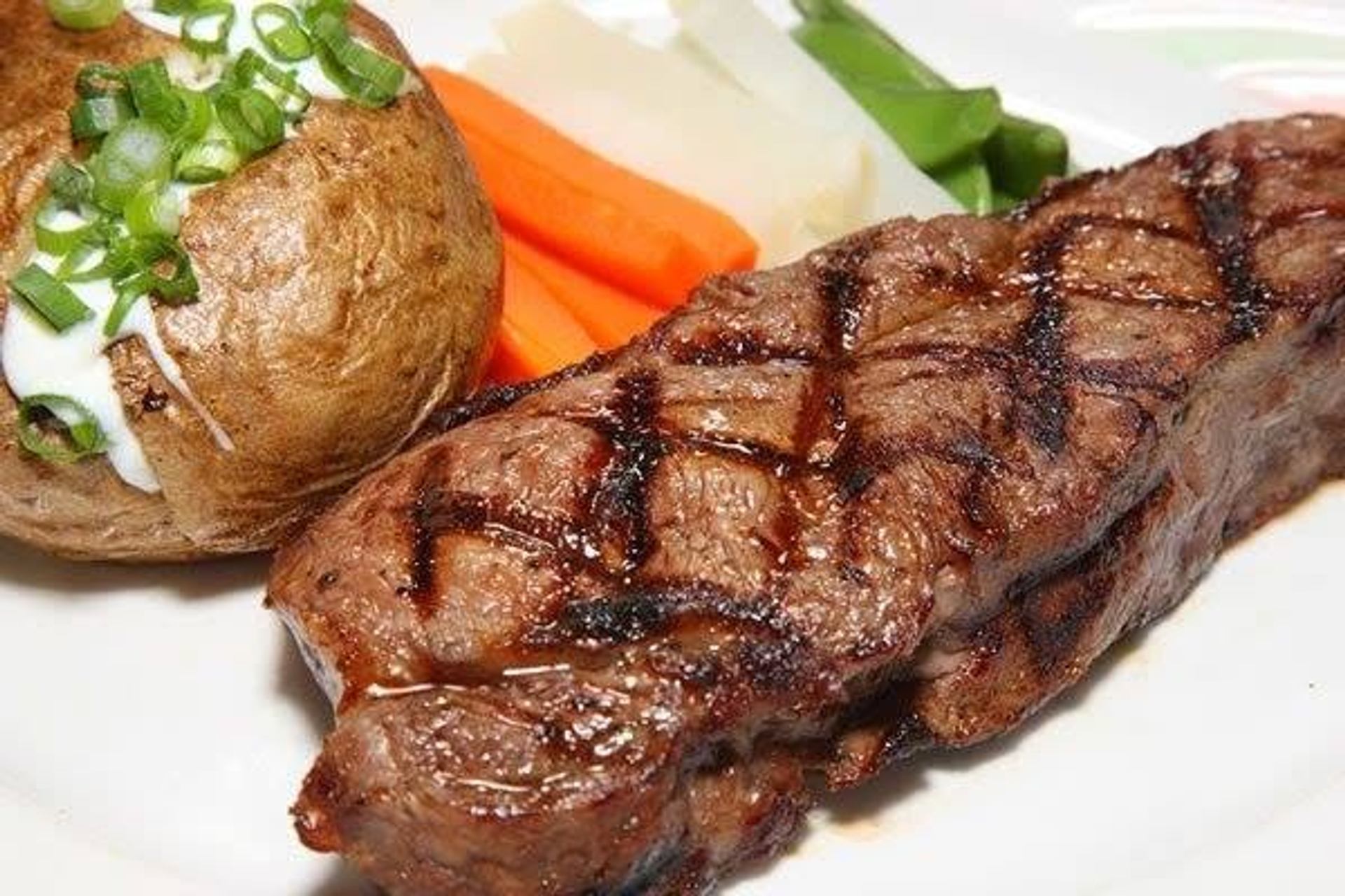 A grilled steak with char marks is served with a baked potato, vegetables, and sour cream.