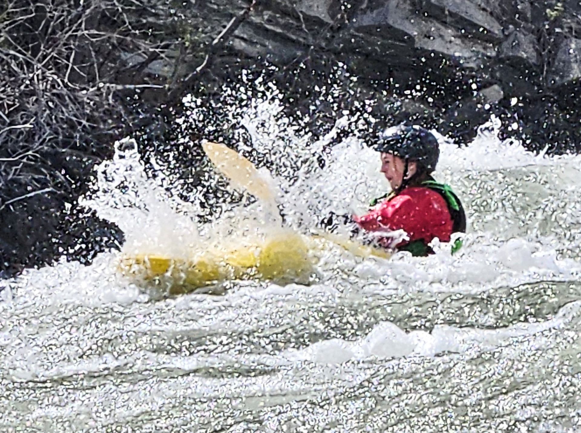 Kayaker navigating fast whitewater as waves splash around the kayak.