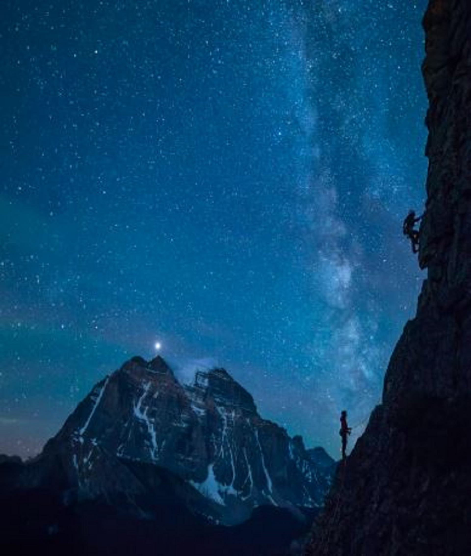 A person climbing a a mountain in the night time with stars in the sky.
