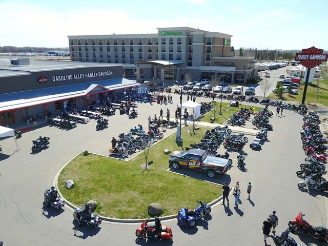 Crowd gathered with rows of Harley‑Davidson motorcycles outside a large dealership.
