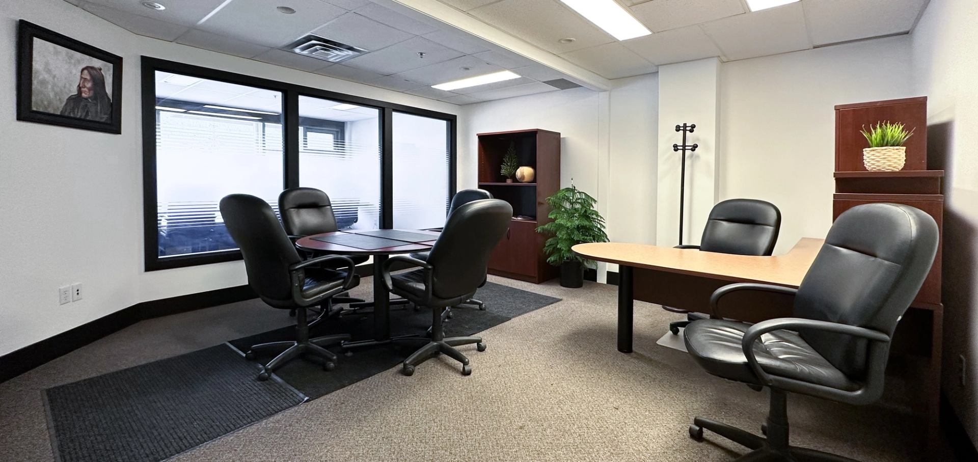 Convertible meeting room or private office set up with a desk and round table, and office chairs.
