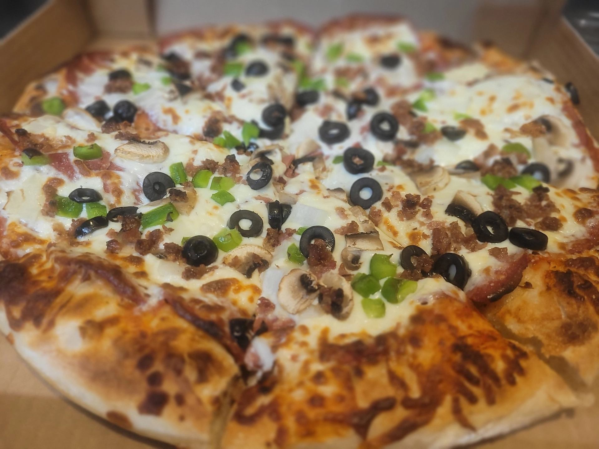 A pizza topped with cheese, black olives, green peppers, mushrooms, and ground meat.
