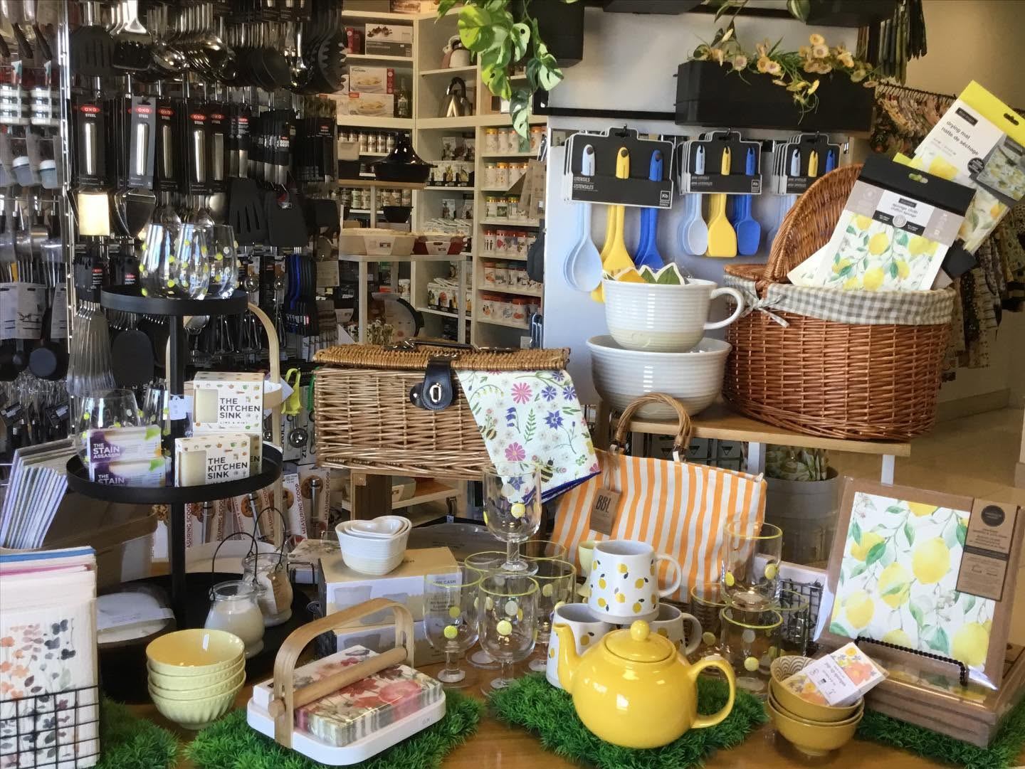 Kitchen store display with yellow teapot, glassware, baskets and hanging utensils on shelves.