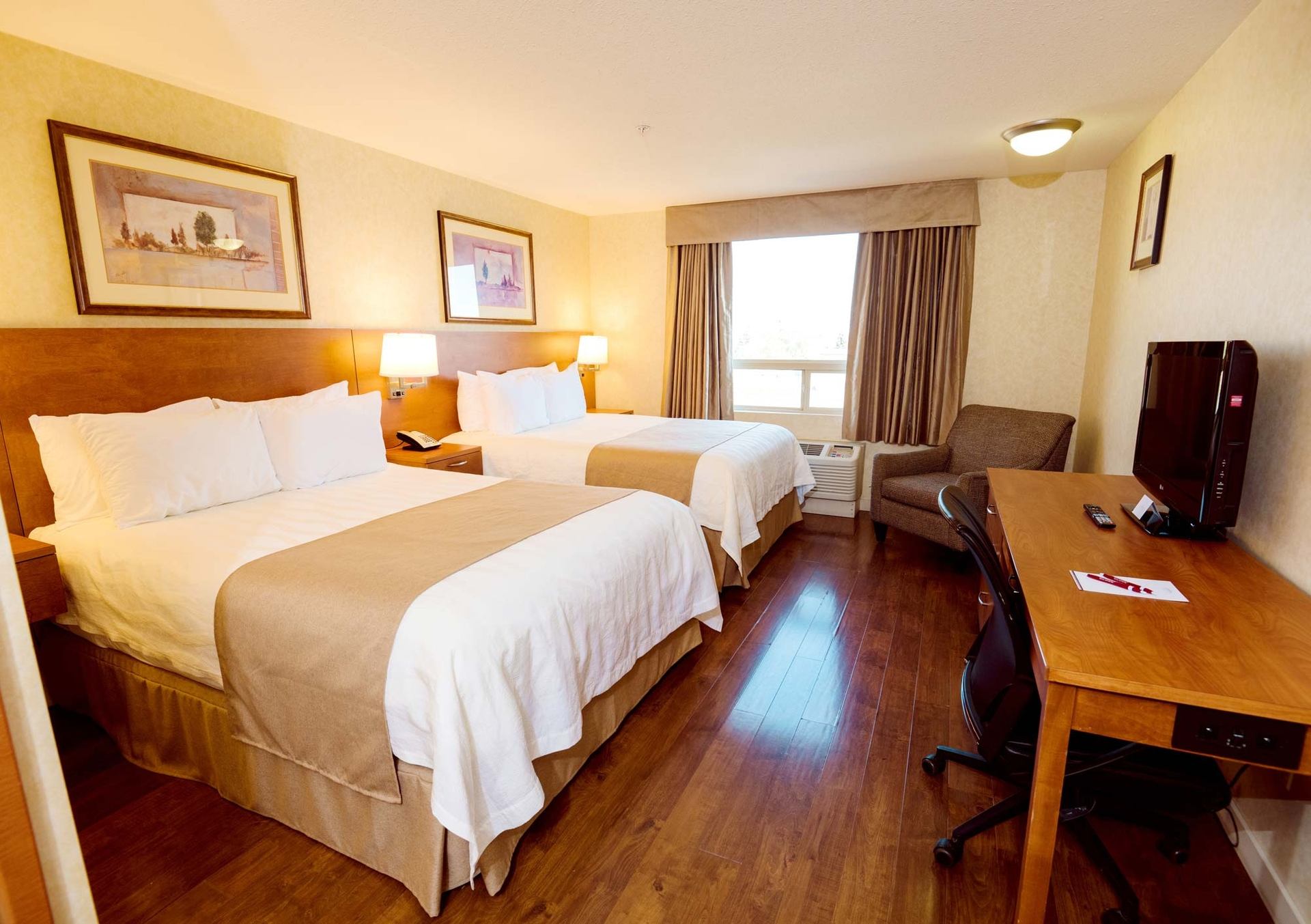 Hotel room with two beds, a desk, television, armchair and window.