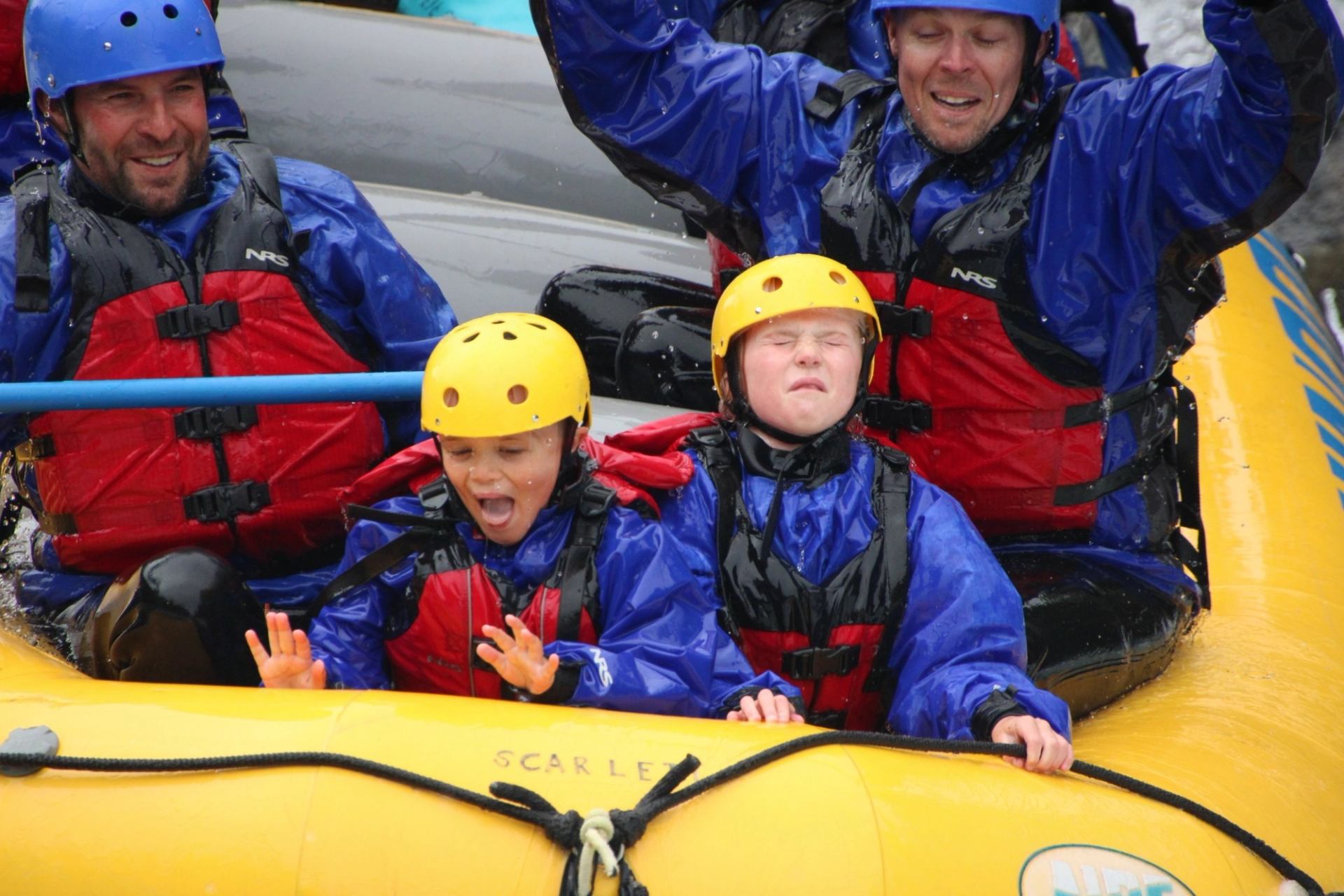 People in helmets and life jackets ride a yellow inflatable rafting boat.