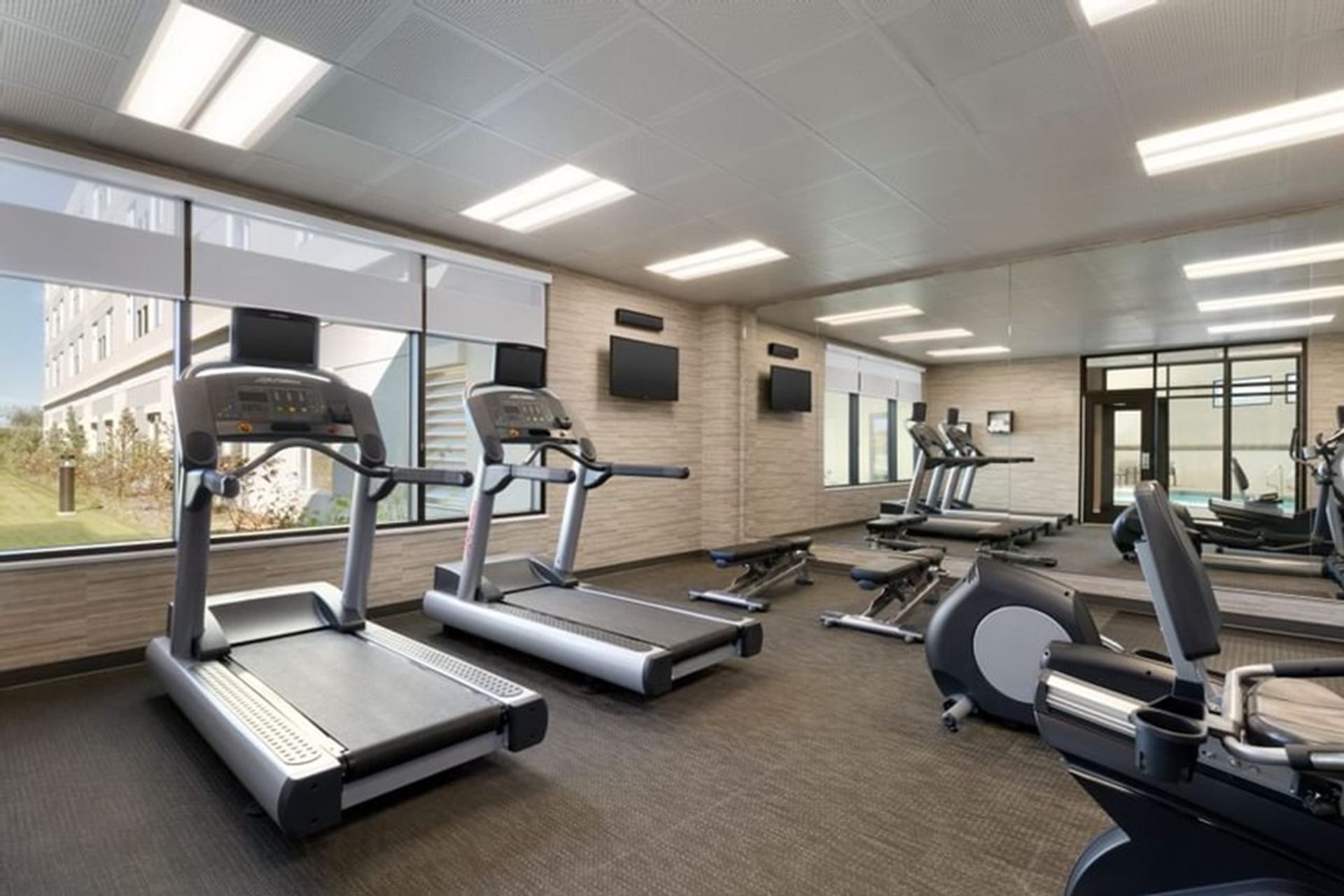 Modern fitness room with treadmills, exercise bikes, weight benches and wall-mounted televisions.
