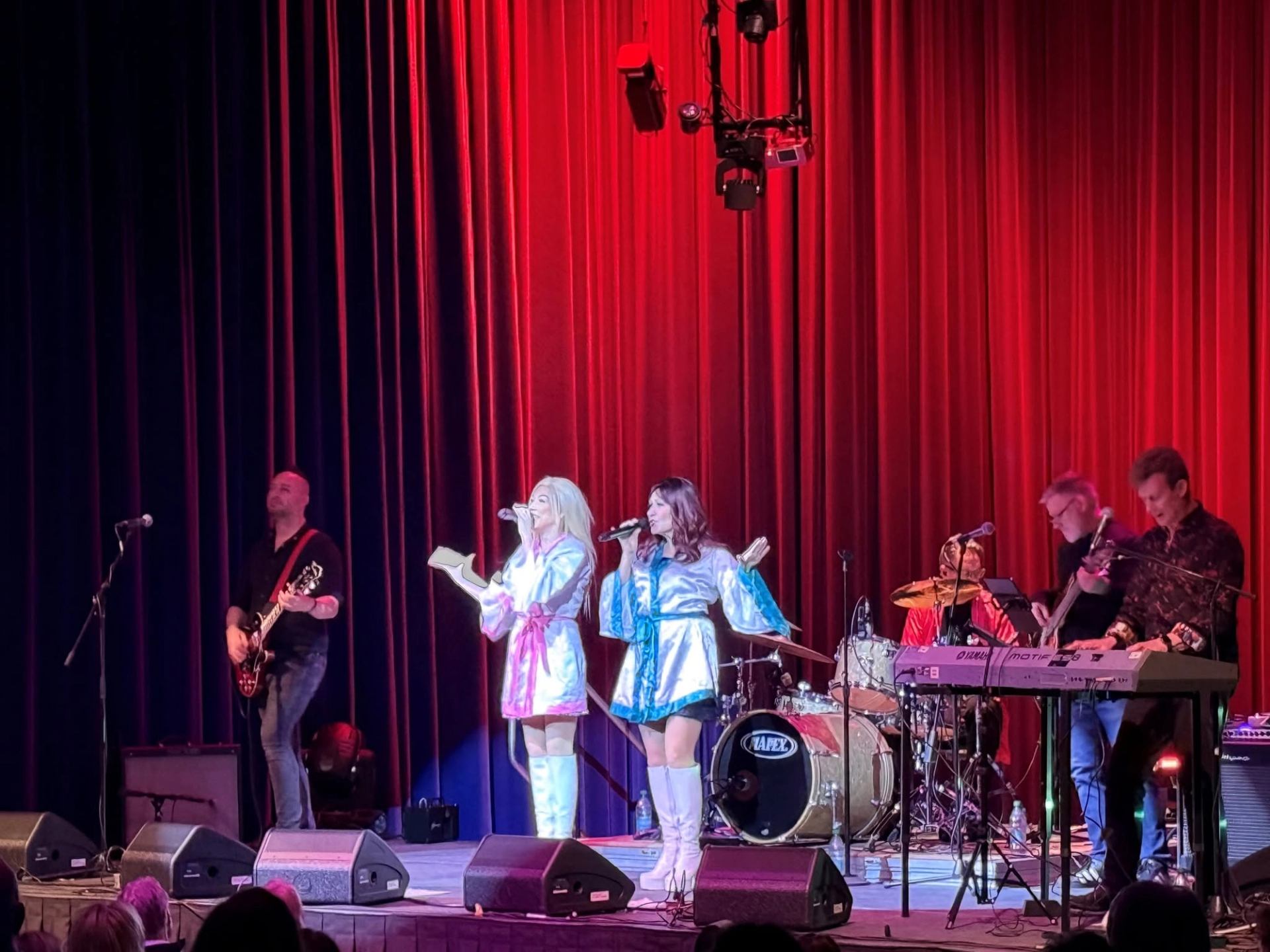 Singers and musicians perform onstage before red theatre curtains.