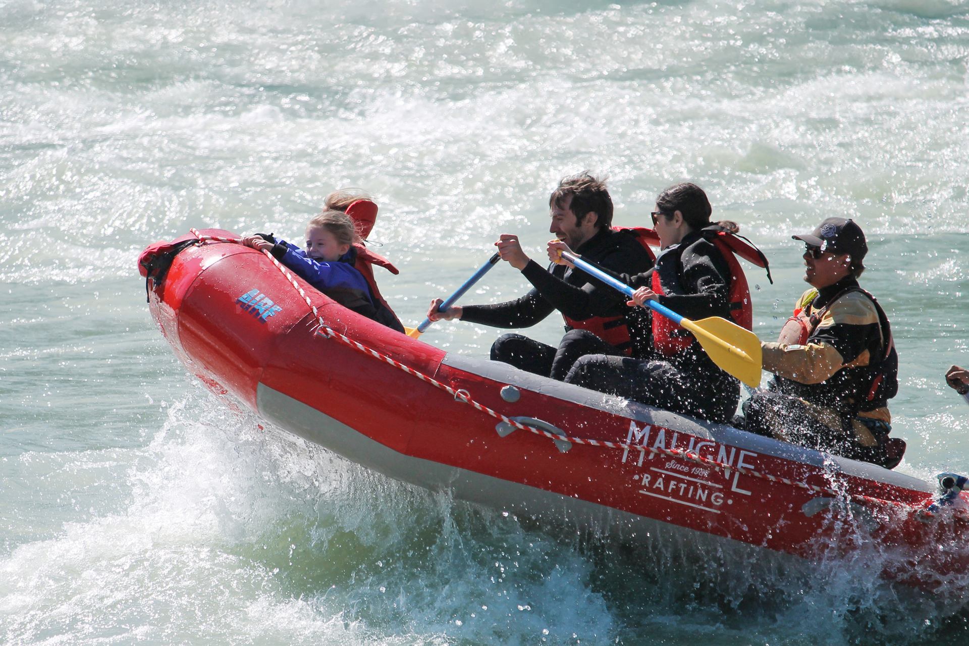 Red raft climbing a wave as the group paddles through strong whitewater.