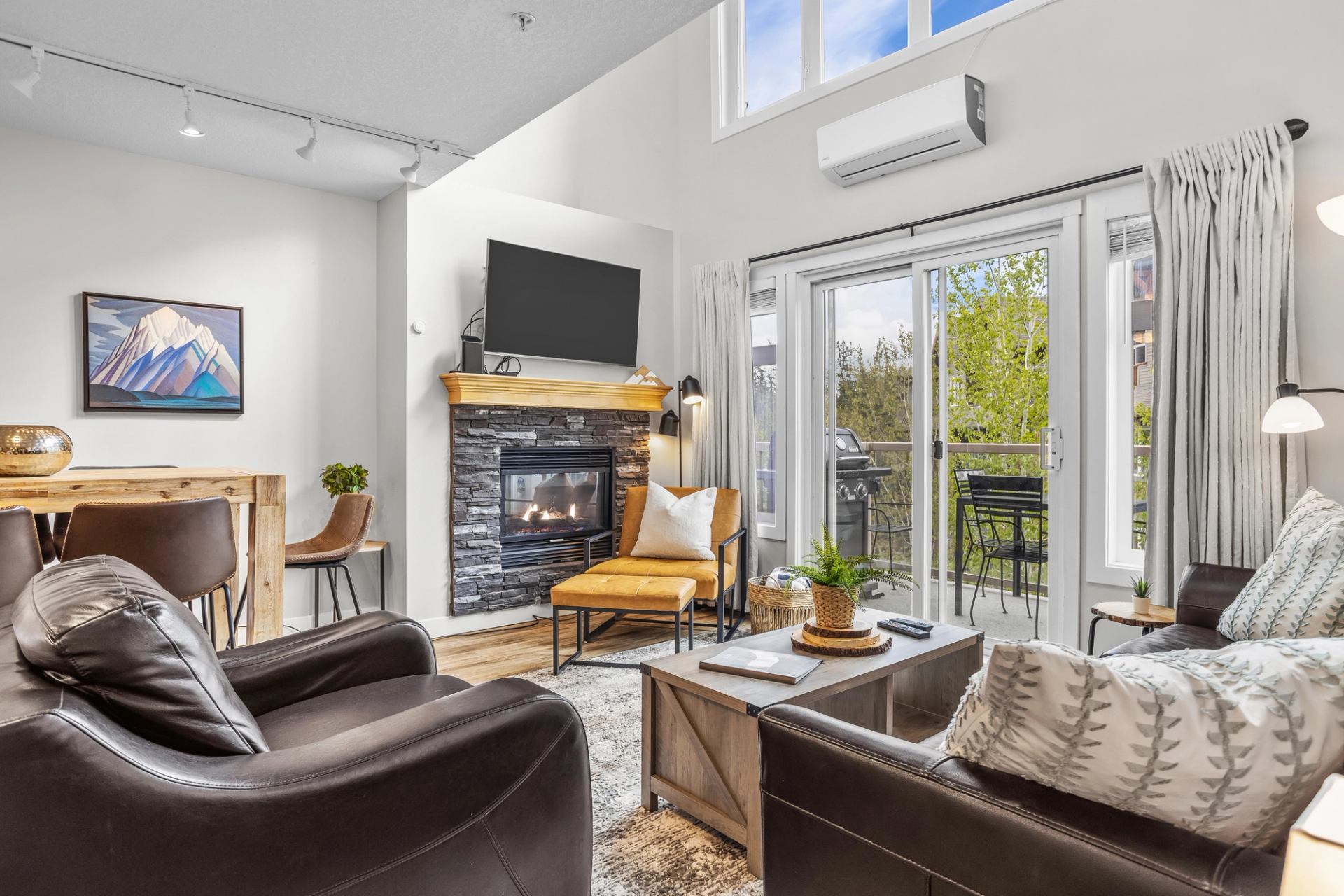 Living room with leather seating, stone fireplace, television and balcony doors.