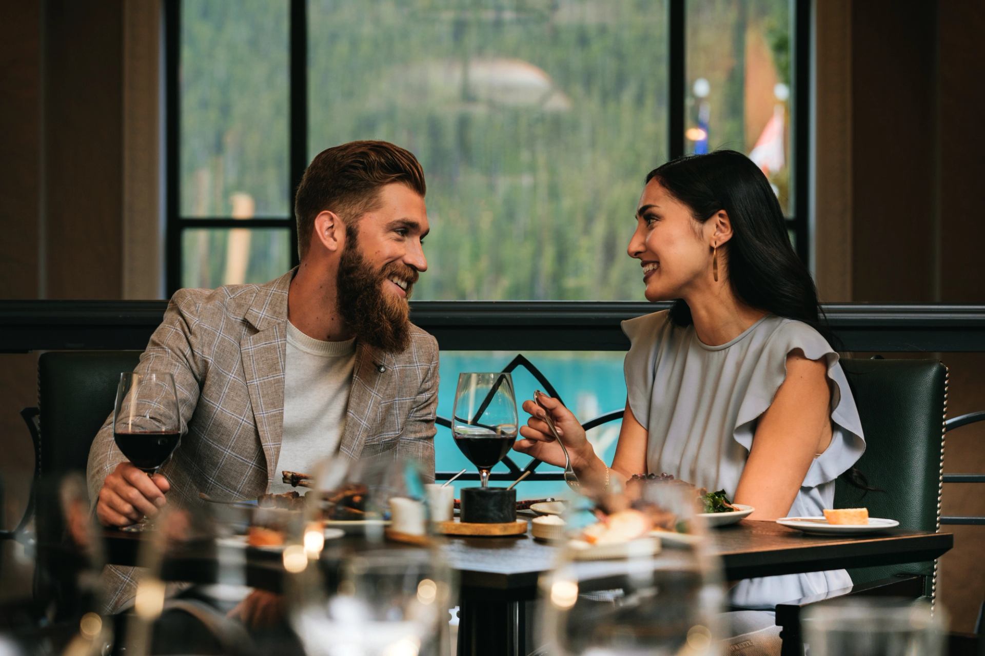 Two people sit at a restaurant table, talking over wine and plated meals.