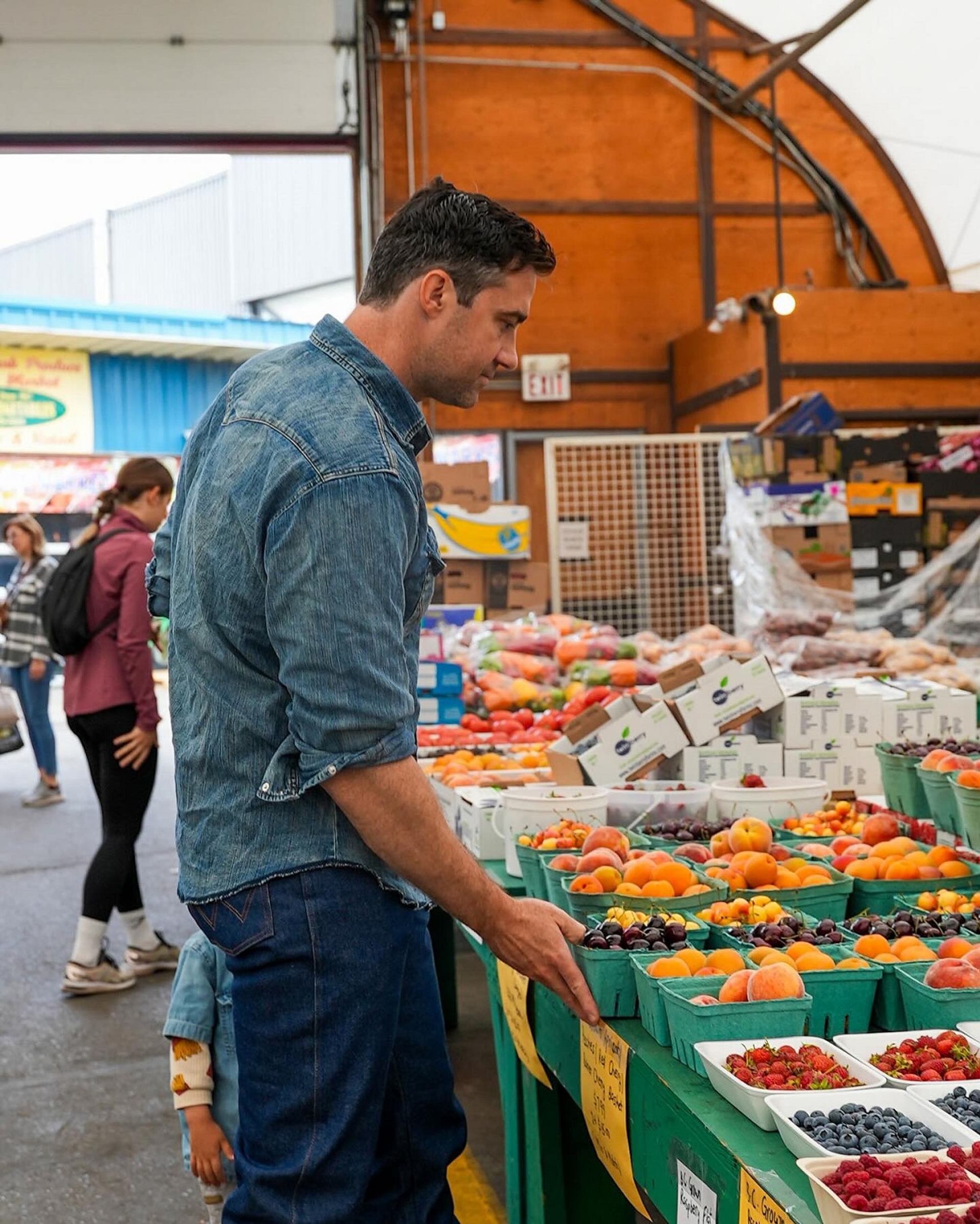 Person browsing colorful berries and fruits at an outdoor produce stand in Crossroads Market.