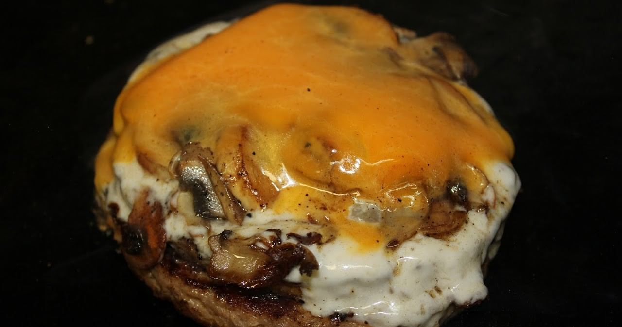 Close-up of a burger patty topped with sautéed mushrooms, Swiss cheese, and melted cheddar.