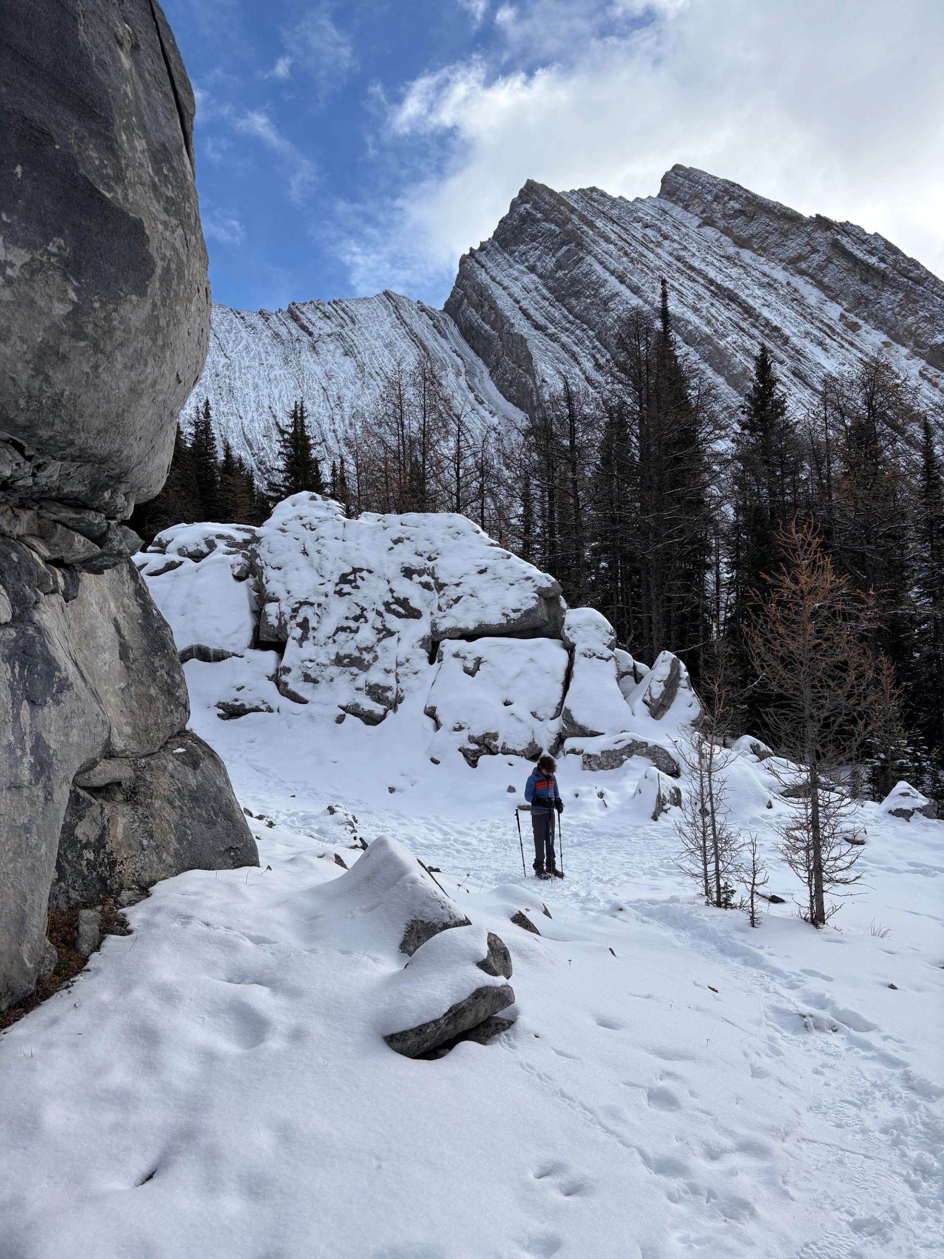 Snowy mountain trail with towering rock formations and evergreen trees.
