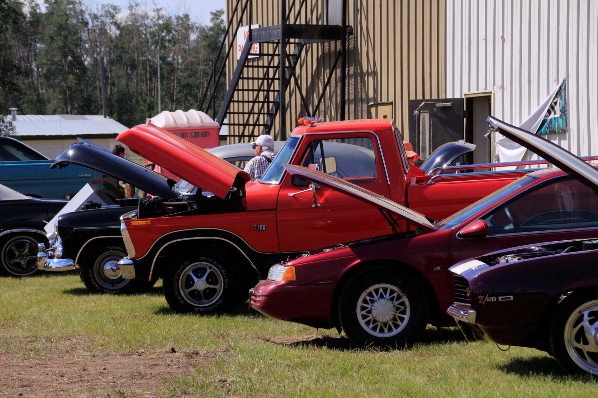 Several classic vehicles parked in a row with their hoods open at an outdoor car show.