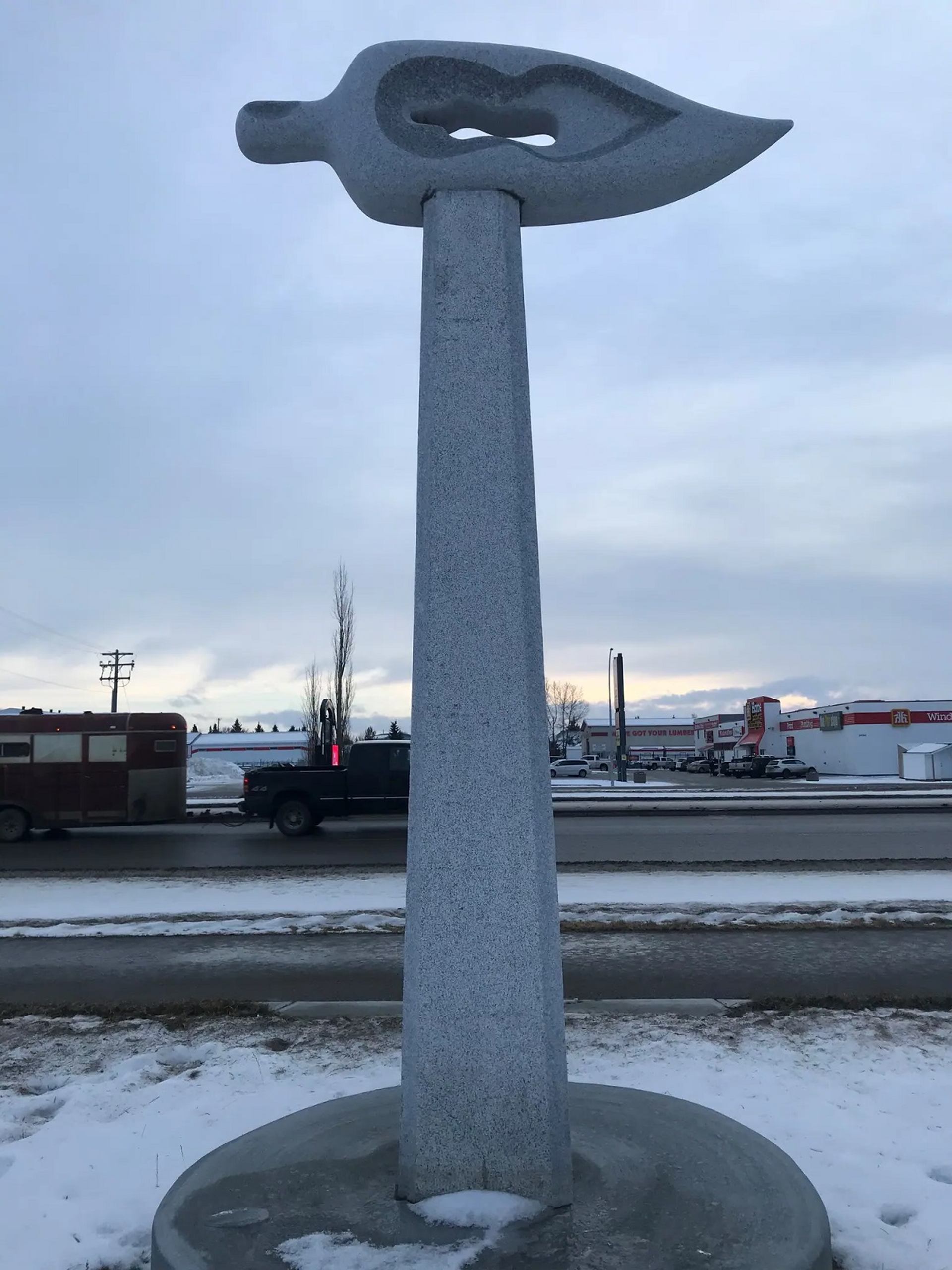 Upright grey sculpture on circular base.