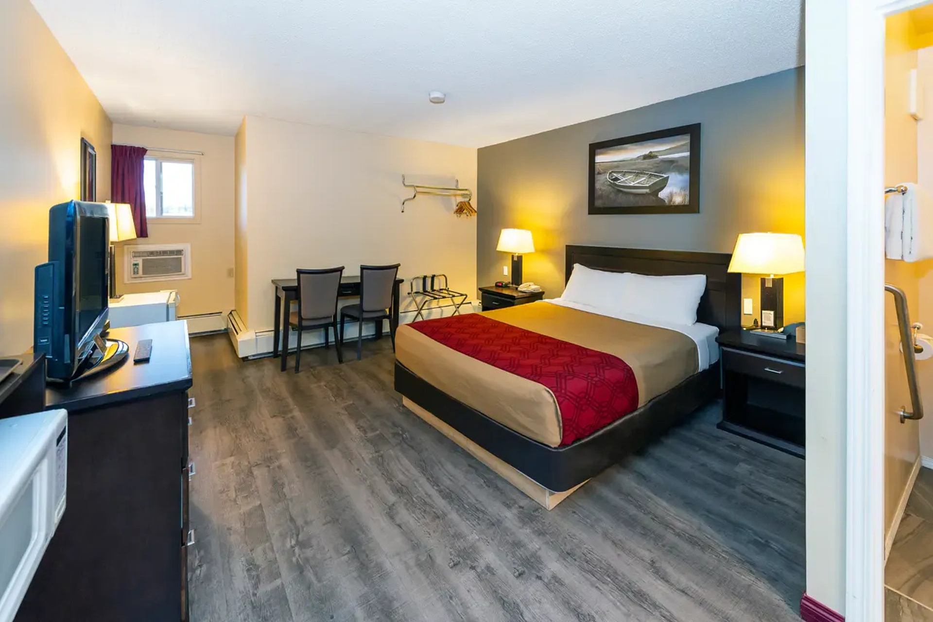 Hotel room with bed, television, desk, chairs, lamps and adjoining bathroom.