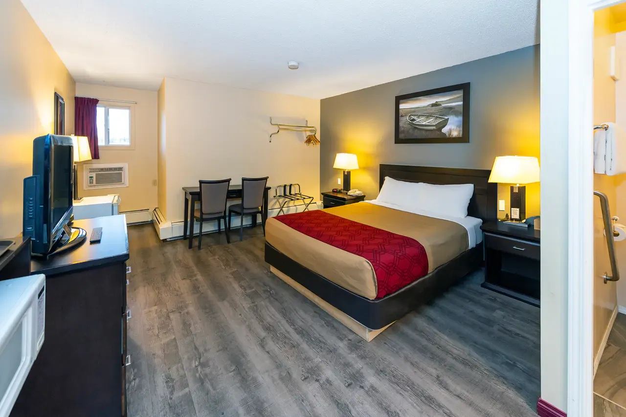Hotel room with bed, television, desk, chairs, lamps and adjoining bathroom.
