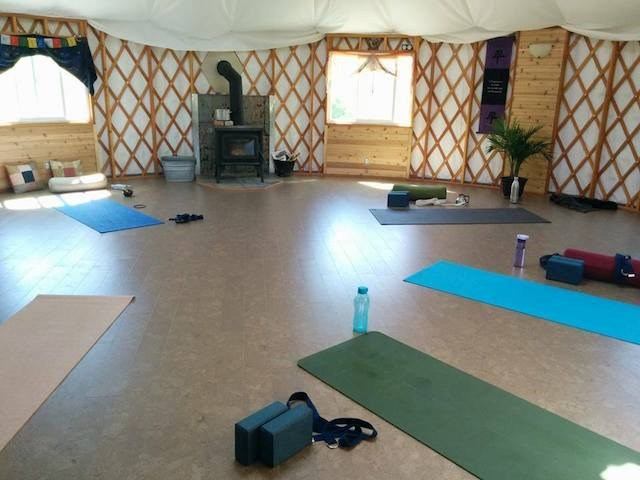 Yoga mats and blocks on floor inside yurt with wood stove and windows.