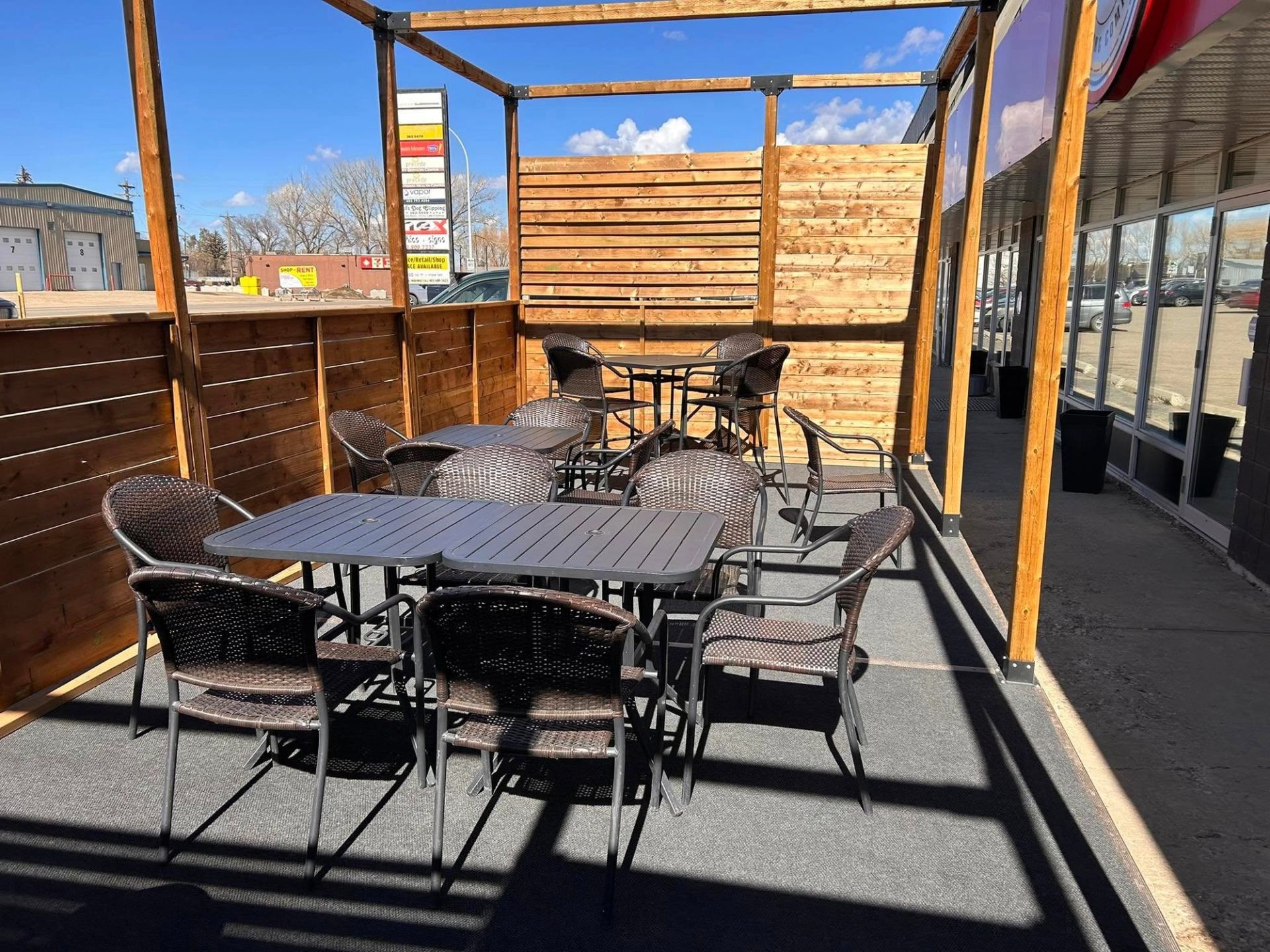 Outdoor patio with wooden panels, tables, and chairs under a clear blue sky.