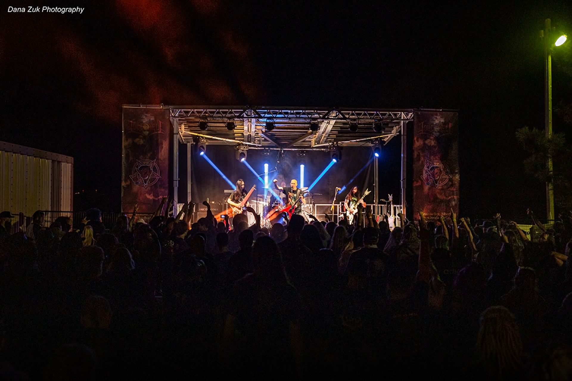 Night concert at Loud As Hell Festival with band performing under bright stage lights and crowd cheering.