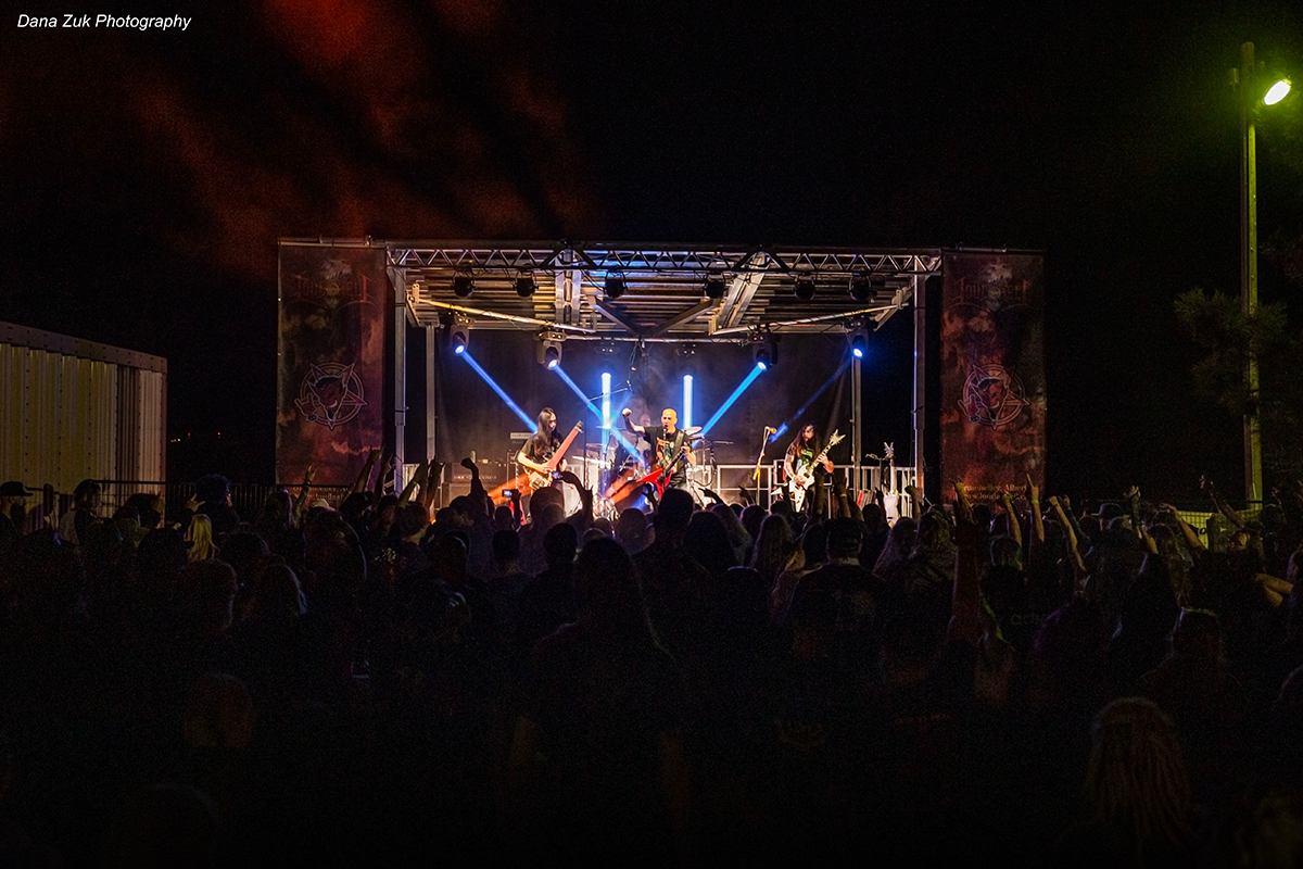 Night concert at Loud As Hell Festival with band performing under bright stage lights and crowd cheering.