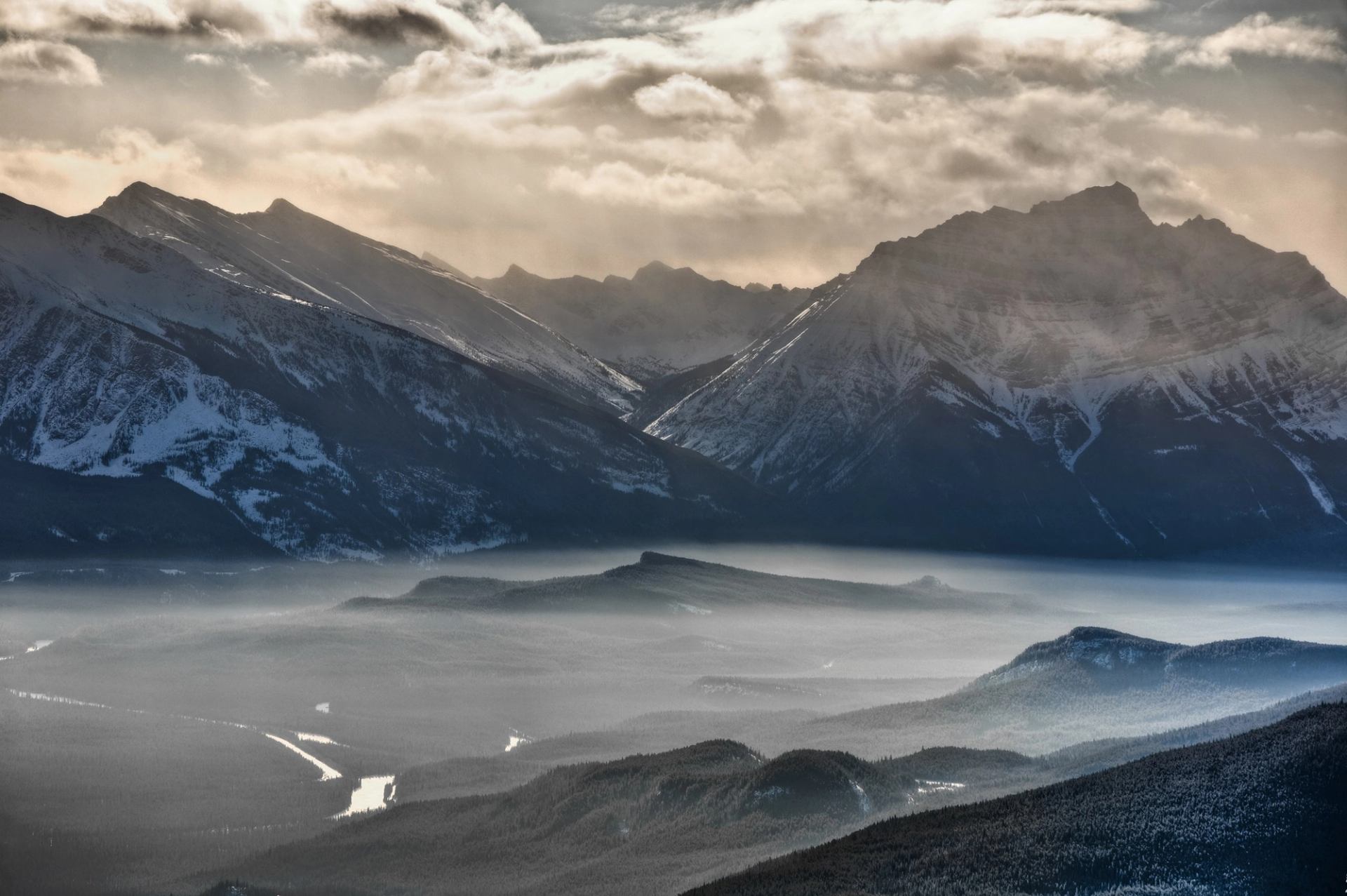 A misty mountain range with snow-covered peaks and valleys beneath a cloudy sky.