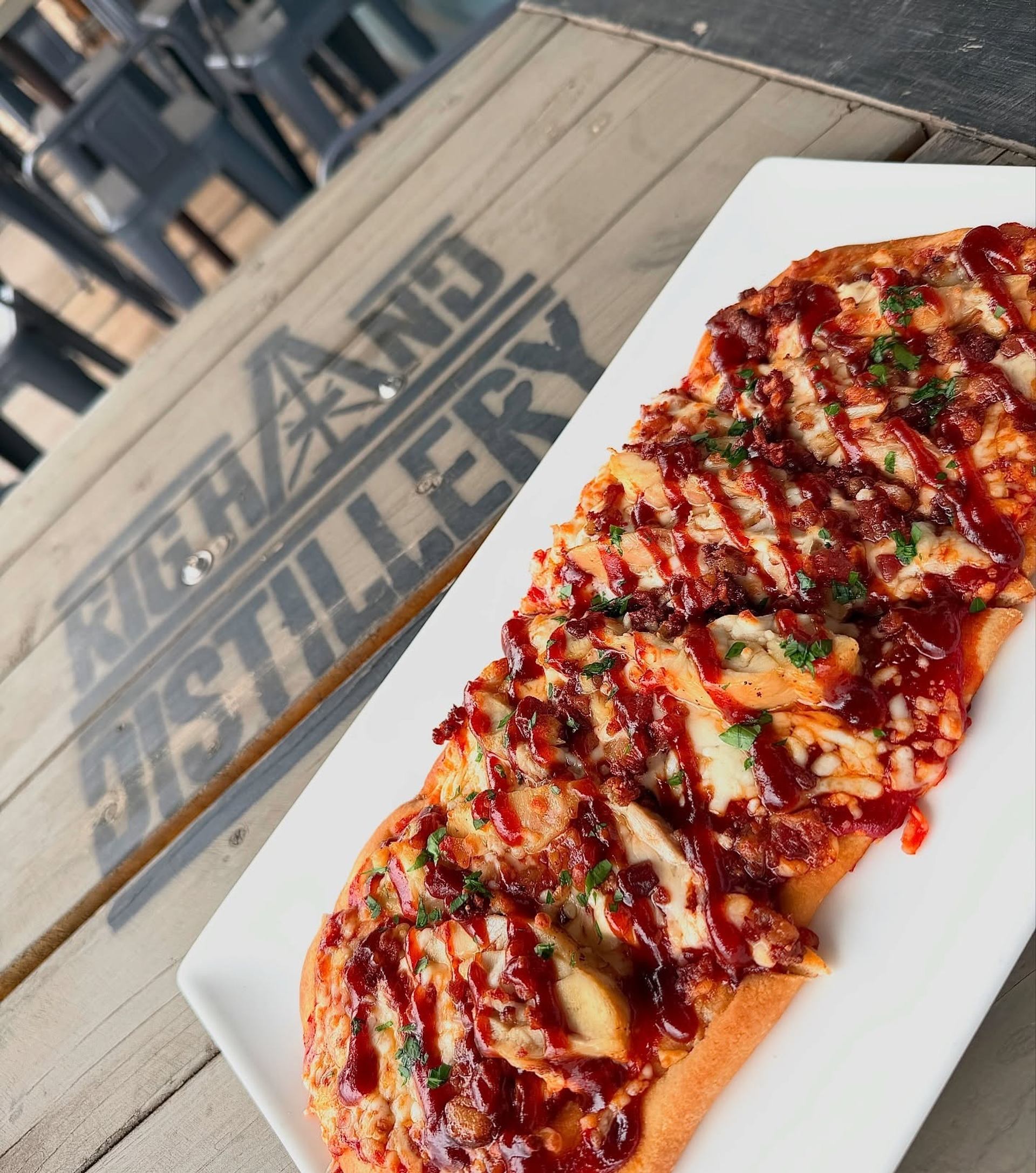 A barbecue-style flatbread topped with cheese and sauce is served on an outdoor patio table.