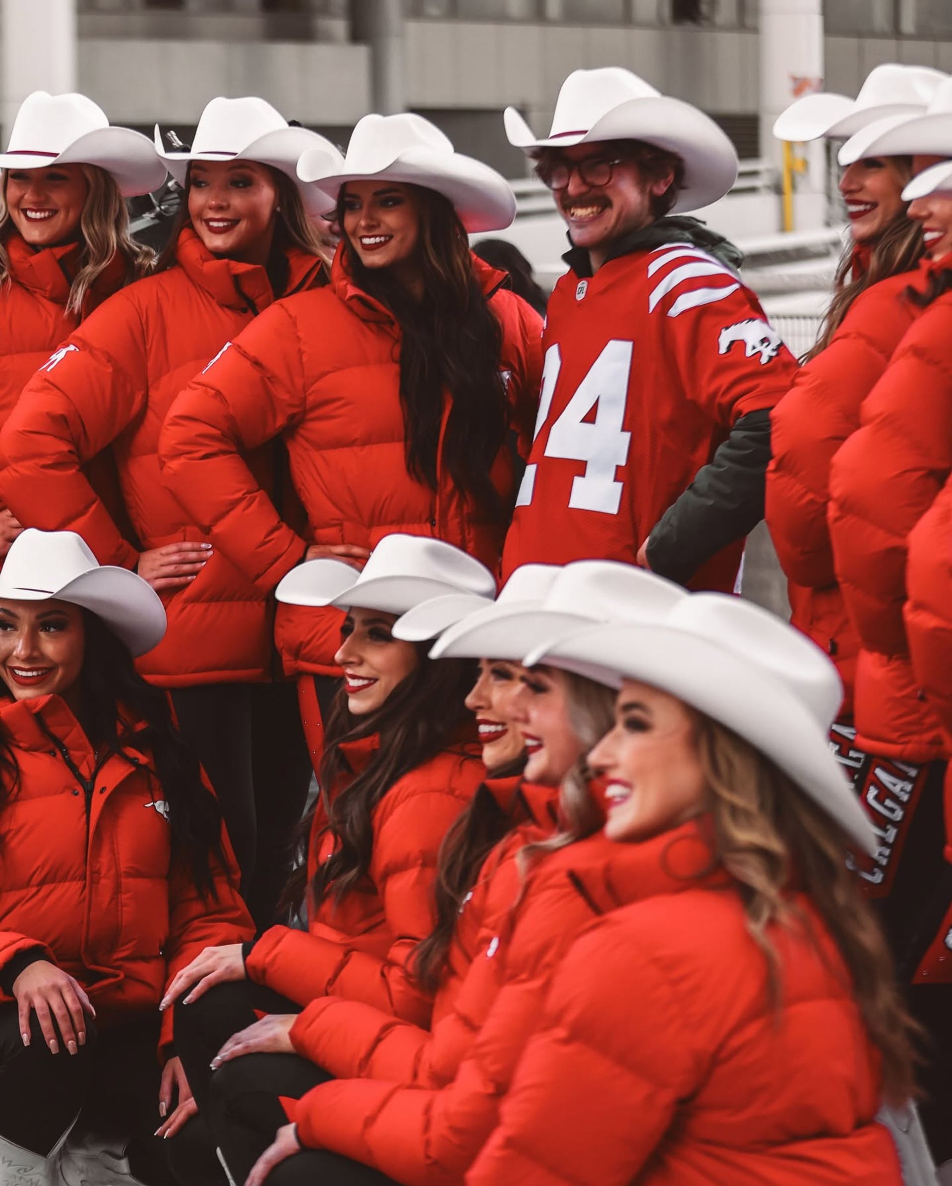 Group in red jackets and white cowboy hats poses with a football fan.