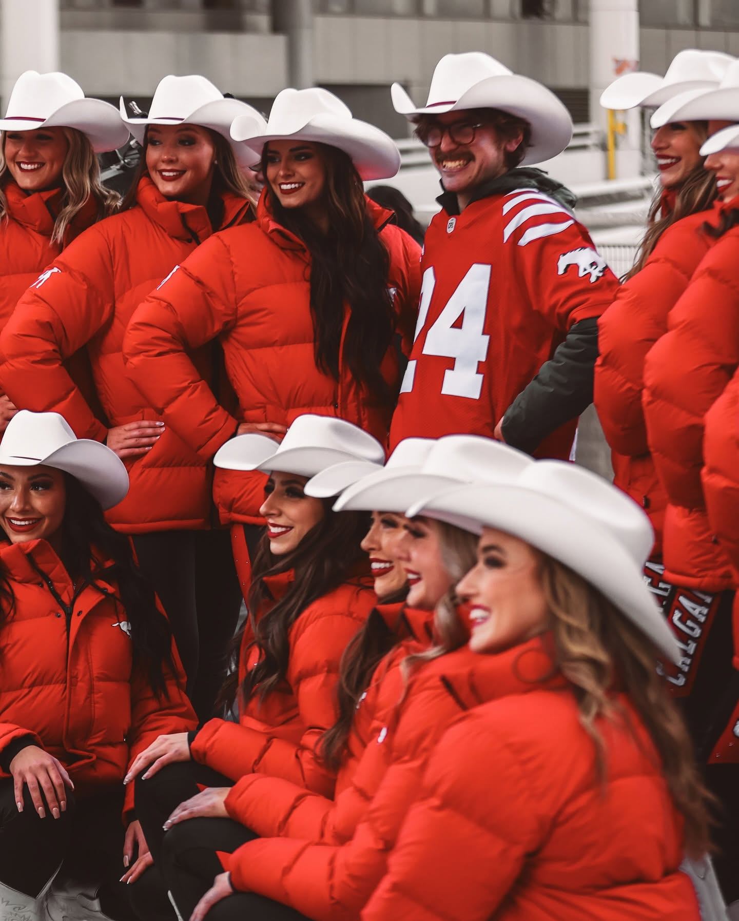Group in red jackets and white cowboy hats poses with a football fan.