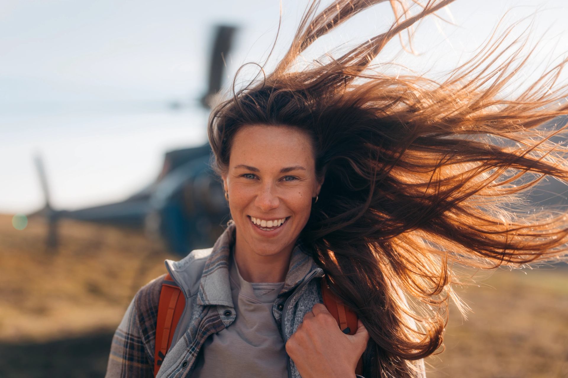 Person standing in a mountain landscape with a helicopter in the background on open terrain.