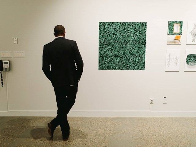 Man in suit viewed from behind standing in art gallery near hanging paintings.
