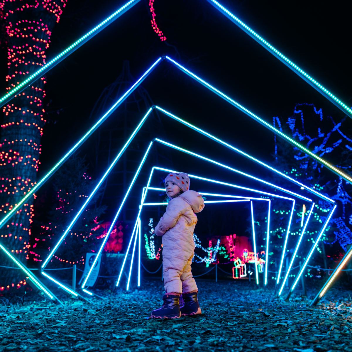 Young child in winter clothes inside a tunnel of blue geometric neon lights