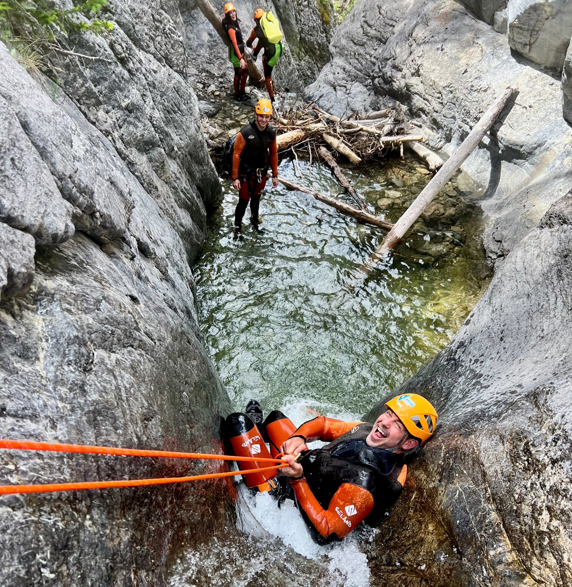 Canyoner gripping ropes in a narrow rocky chute with teammates in Bow Valley.