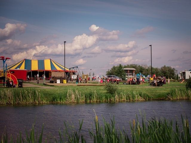 Striped event tent and activities near pond at Cecil Thompson Park campground