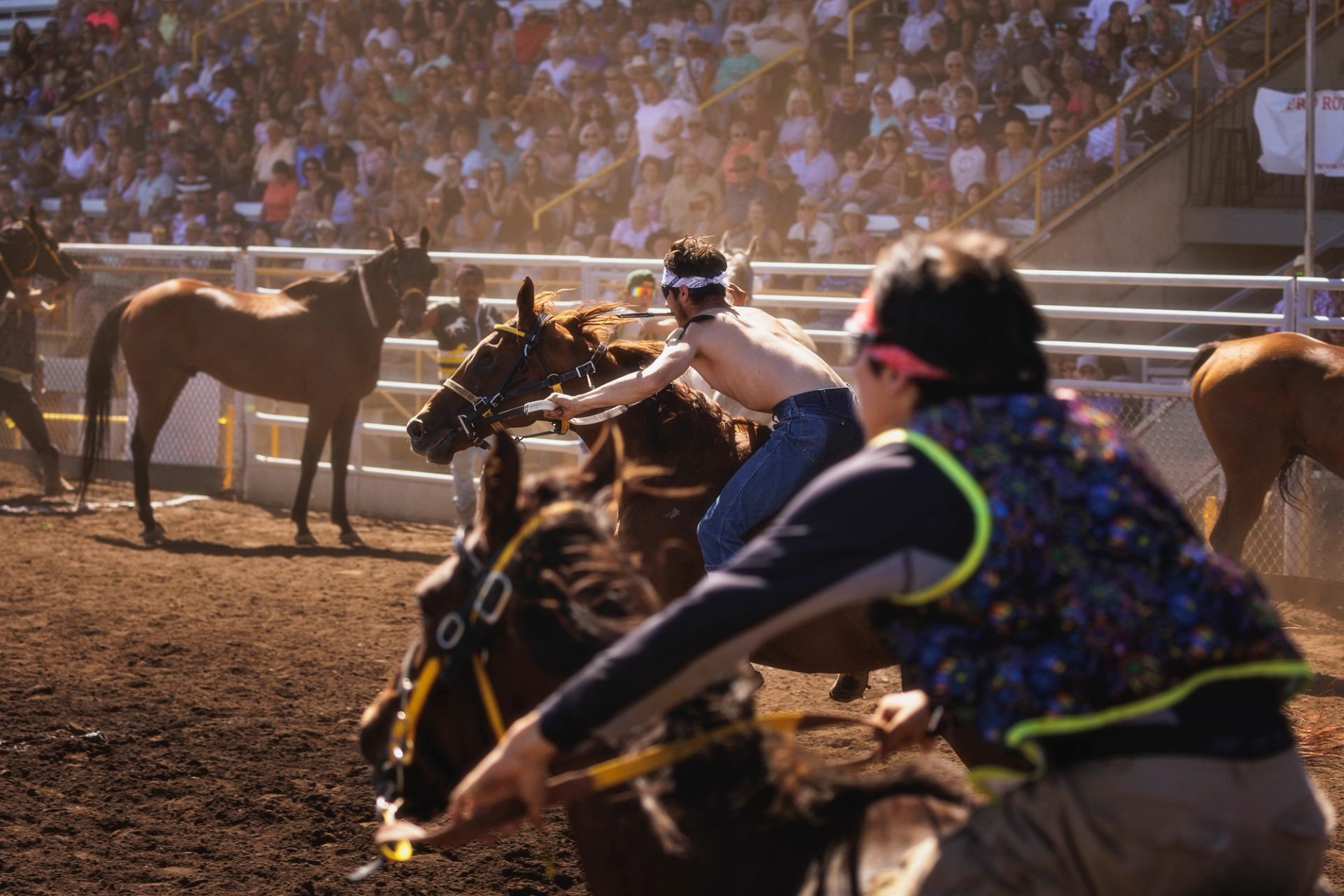 Bare-chested rider leans forward on galloping horse during dirt track race before crowd.