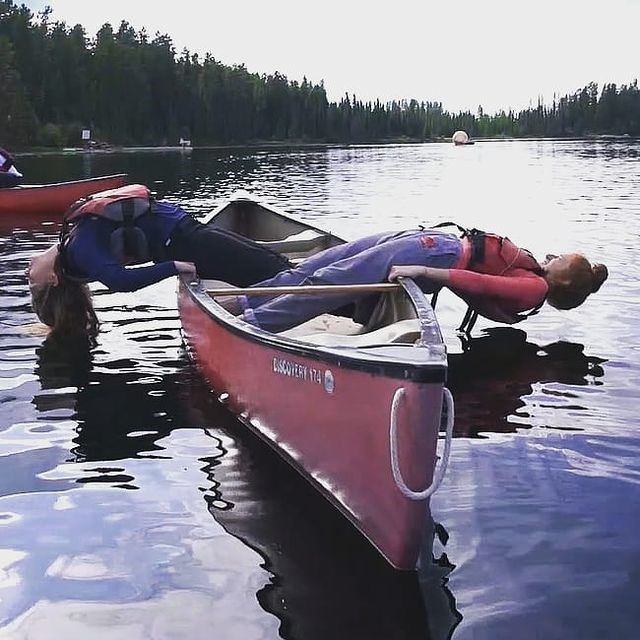 Two people balance on a canoe in a lake at HeLa Ventures.