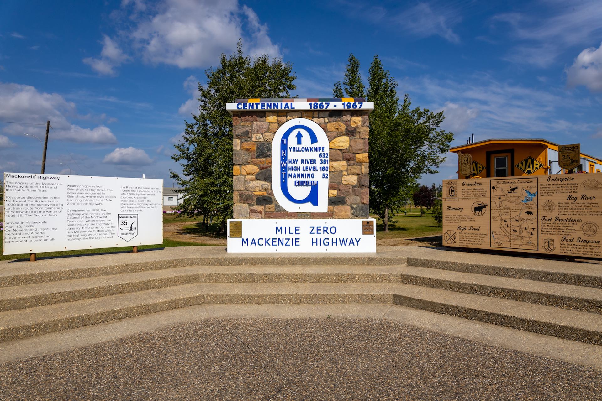 Stone monument marked Mile Zero Mackenzie Highway with informational signs and trees.