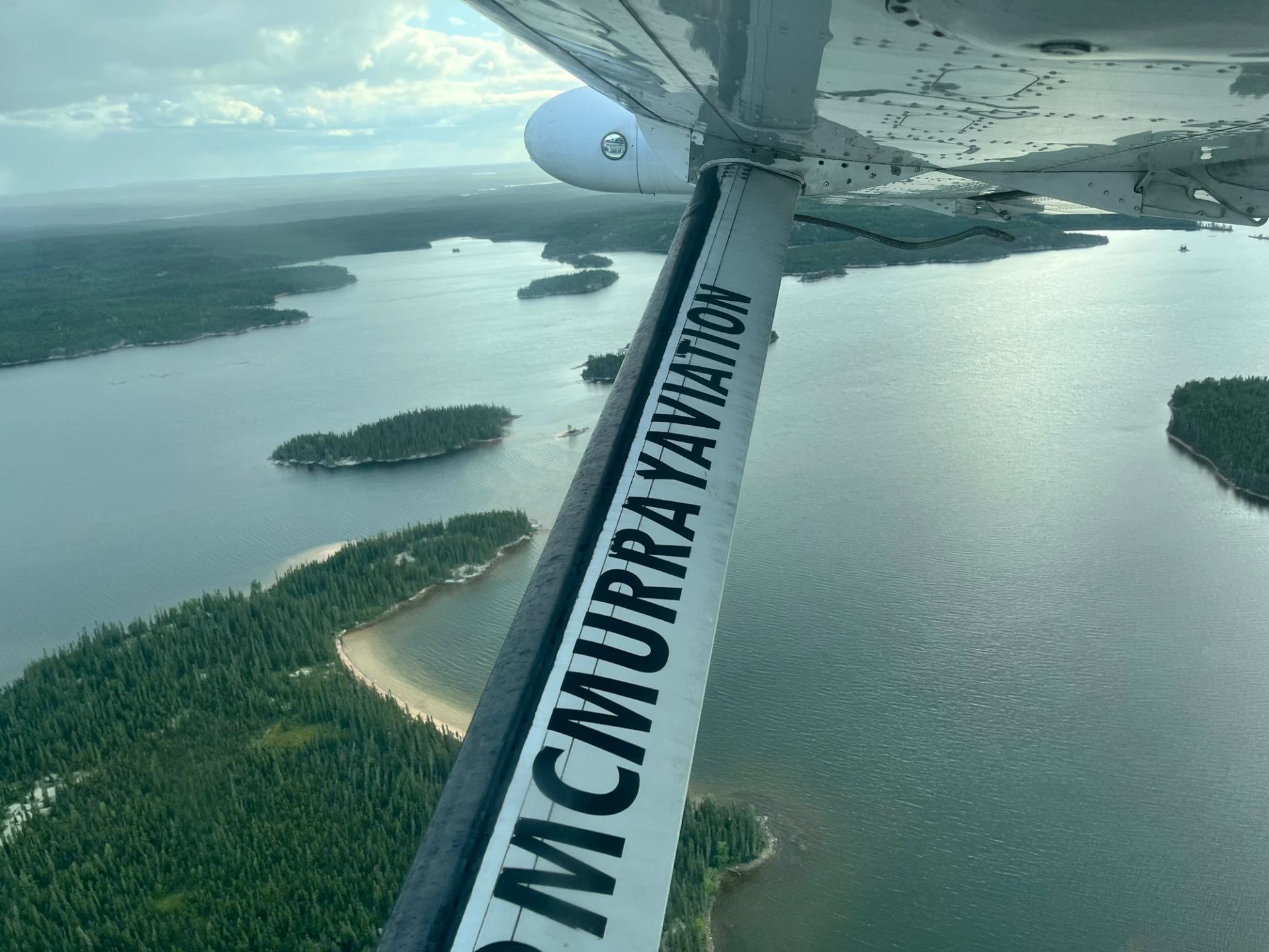 Aerial view from plane with “McMurray Aviation” wing over water and islands.