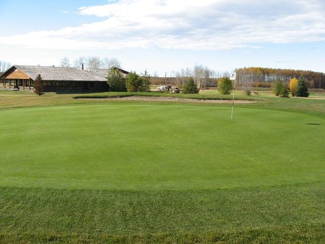 Wide view of a golf green with a clubhouse and trees in the background at Fox Haven Golf & Country Club.