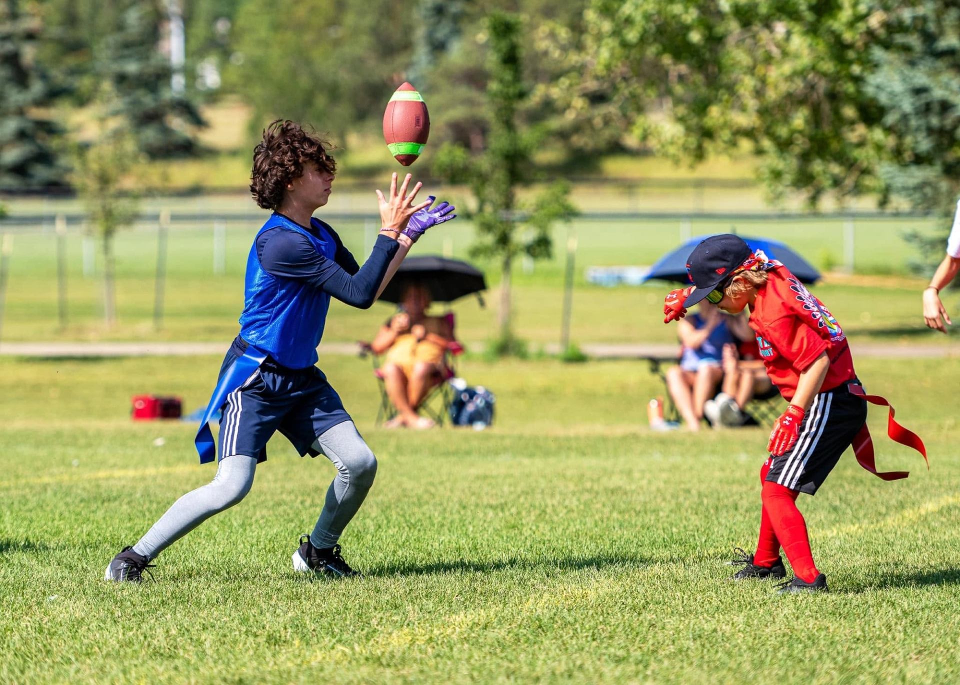 Youth flag football players on grass field as one prepares to catch ball mid-air.