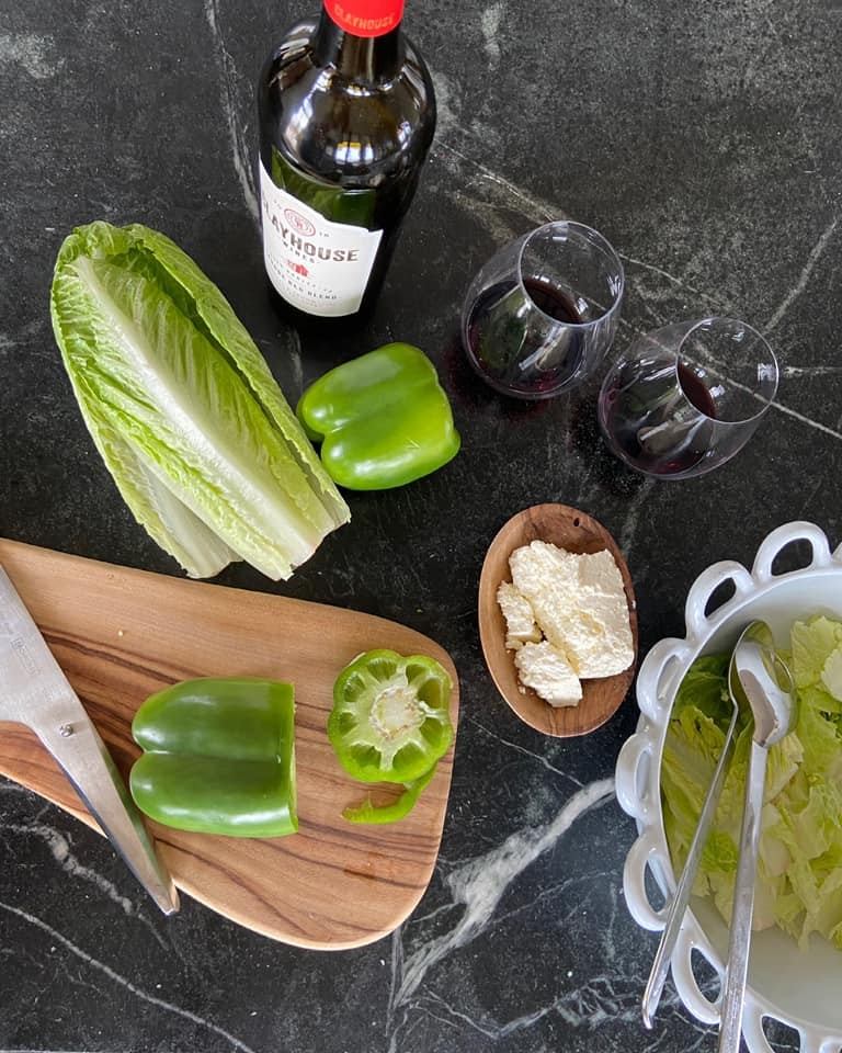 Fresh green pepper, lettuce, wine, and cheese arranged on a dark kitchen counter.