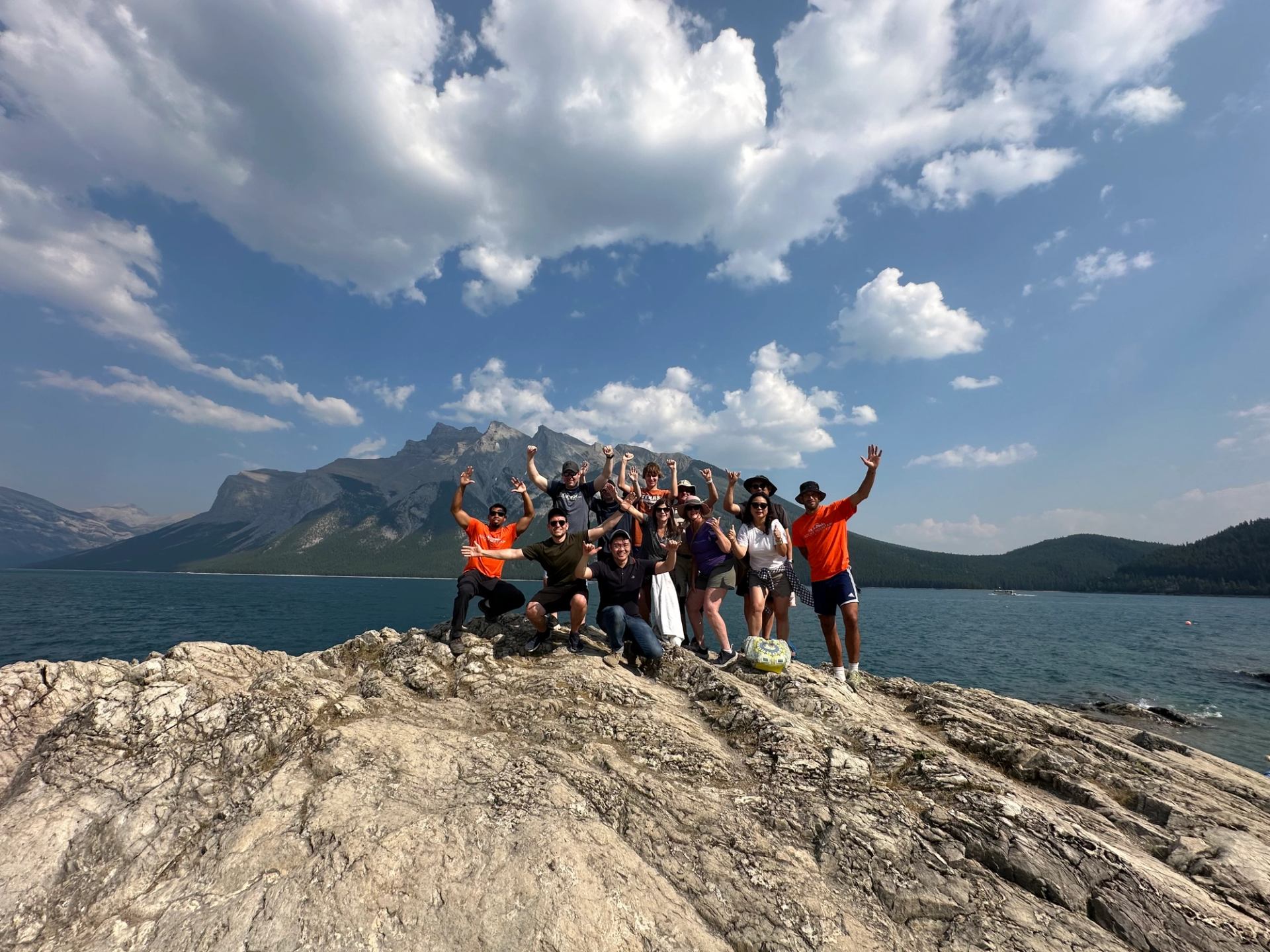 Group standing on rocky shoreline with Lake Minnewanka and mountains behind them.