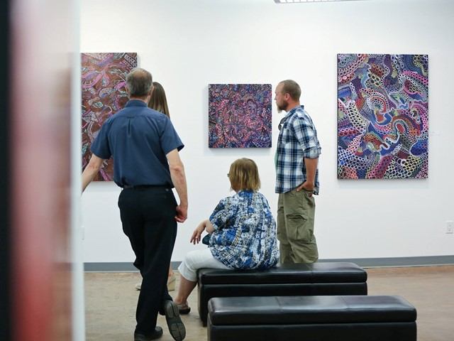 People view abstract paintings in an art gallery with a bench in the foreground.