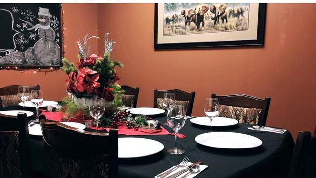 Dining table with red floral centrepiece, set plates, wine glasses and cutlery.