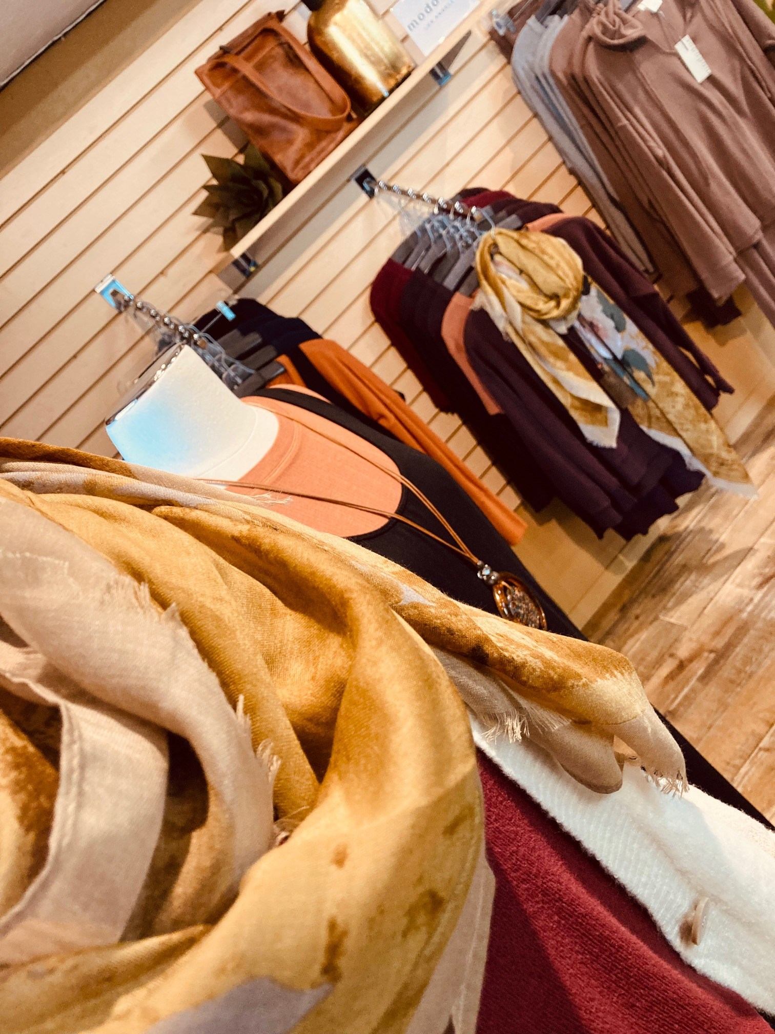 Clothing rack display with folded sweaters, scarves, and shirts for sale in a retail store.