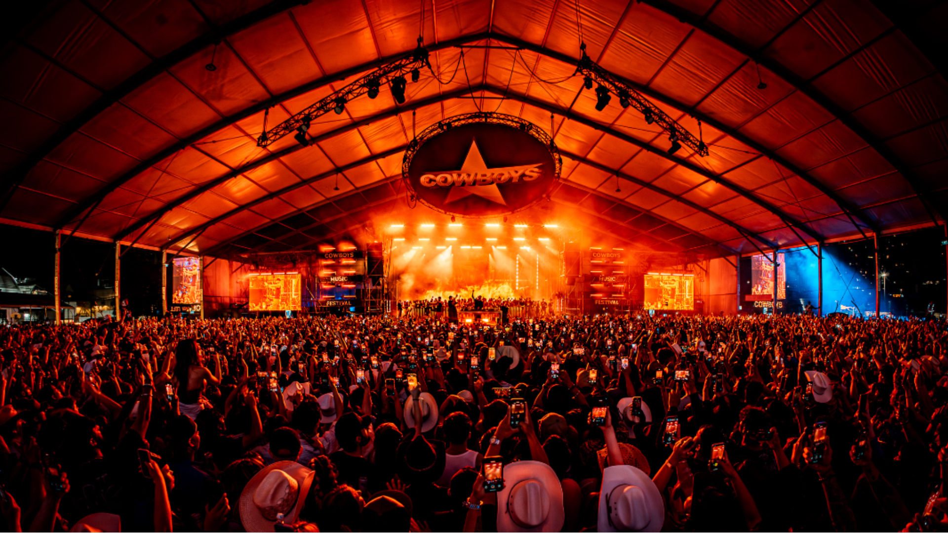 Packed festival crowd facing a glowing orange stage at night