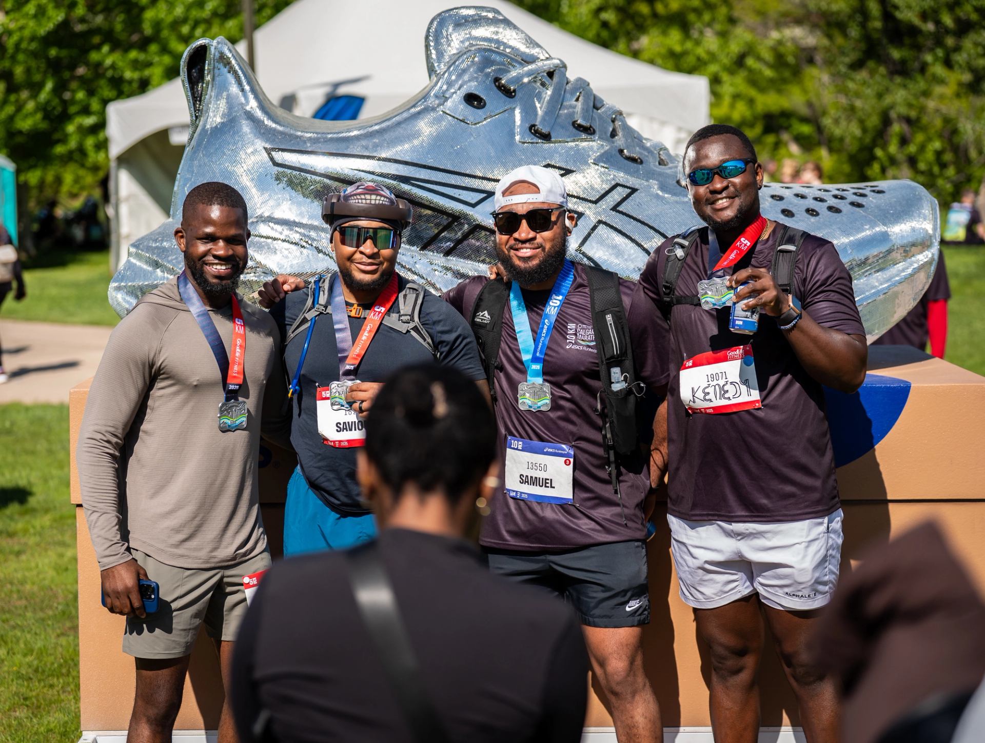 Runners wearing medals pose in front of oversized silver shoe display.