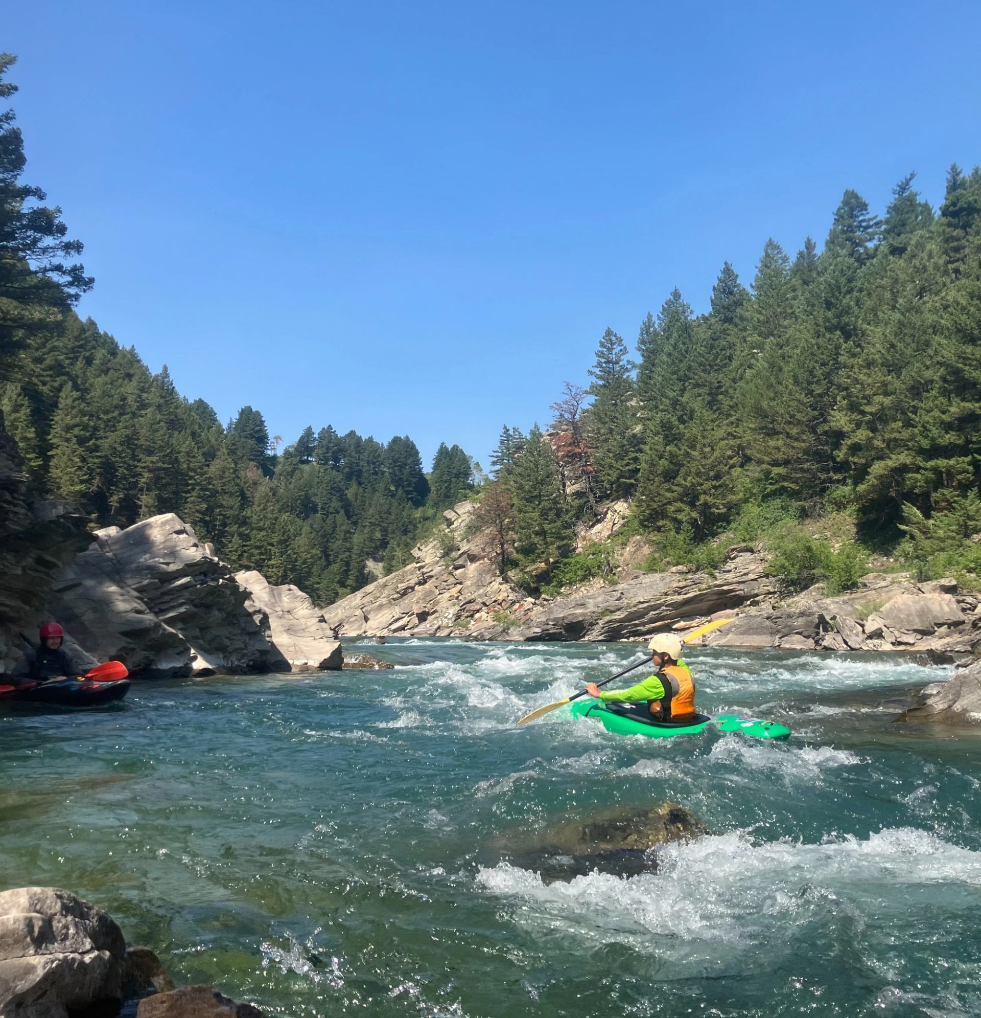 Kayaker in a green kayak navigating a clear river through forested canyon walls.