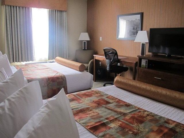 Hotel room with two beds, desk and chair, TV on dresser, curtained window.