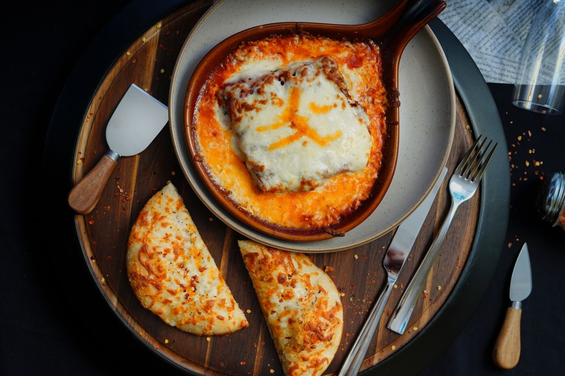 Cheese-covered baked dish in a handled pan with two folded flatbreads.